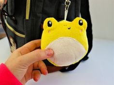 a hand holding a small yellow animal keychain in front of a black backpack