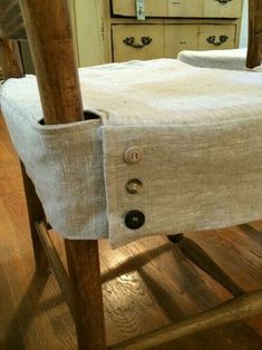 an old wooden chair with a white table cloth on it's seat and button holes in the back