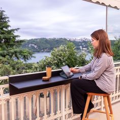 a woman sitting at a table on top of a balcony using a laptop computer next to a cup of coffee