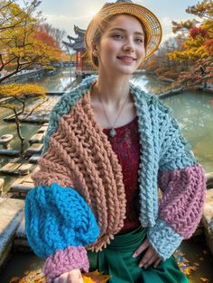 a woman wearing a hat and sweater sitting on a bench in front of a pond