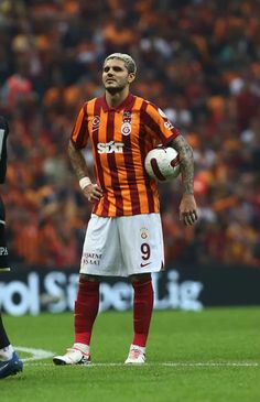 a man standing on top of a soccer field holding a white and orange ball in his hand