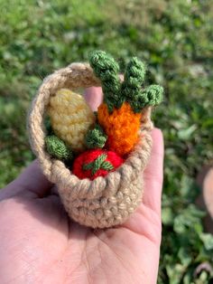 a hand holding a small crocheted basket with fruits and vegetables in it on the grass