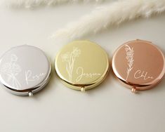 three personalized compact mirrors sitting next to each other on a white surface with feathers