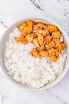 a white bowl filled with rice and chicken on top of a marble countertop next to a fork