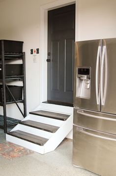 a refrigerator and stairs in a room with white walls, carpeted flooring and black doors