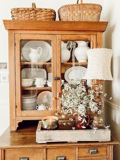 a hutch with dishes and baskets on it, sitting next to a table lamp