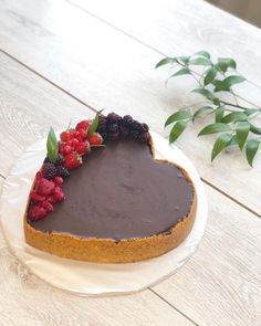 a heart - shaped chocolate cake with berries on top sits on a plate next to a plant