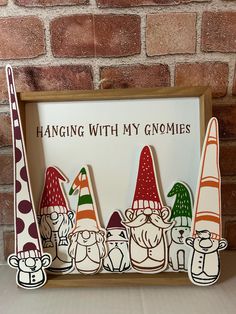 a wooden sign with gnomes on it sitting in front of a brick wall that says hanging with my gnomes