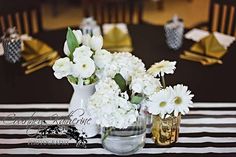 white flowers are in vases on a black and white striped tablecloth with gold place settings