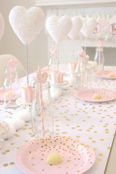 a table set up for a baby shower with pink and gold plates, candy lollipops, and heart shaped balloons