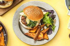 a burger and some fries on a plate next to a bowl of potato wedges