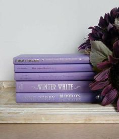 three purple books sitting on top of a wooden shelf next to a bouquet of flowers