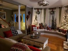 a living room filled with furniture and christmas trees in the window sill, surrounded by holiday decorations