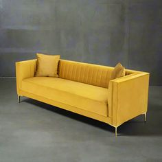 a yellow couch sitting on top of a floor next to a gray wall and two brown pillows