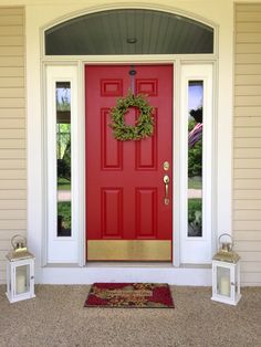 a red front door with two white lanterns and a wreath on the side of it