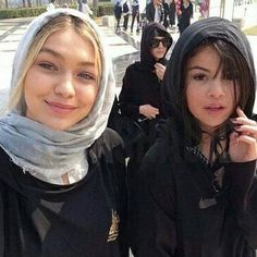 two young women standing next to each other with headscarves on and one holding a cell phone