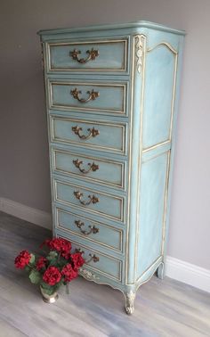 a blue chest of drawers sitting on top of a hard wood floor next to a vase with red flowers