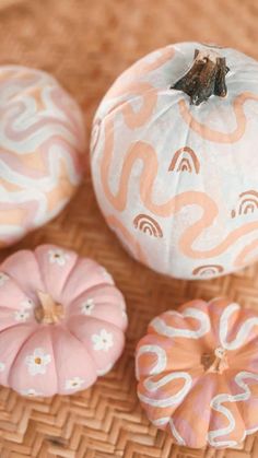 three painted pumpkins sitting on top of a woven table cloth next to each other