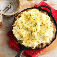 a skillet filled with mashed potatoes on top of a red napkin next to a glass of beer