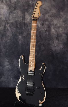 an old black guitar is sitting on a stand in front of a dark background with scratches