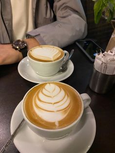 two cups of cappuccino sitting on top of a table next to each other