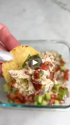 a hand holding a tortilla chip with chicken salad in it