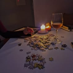 a candle is lit on a table with puzzle pieces in front of it and a glass of wine next to it