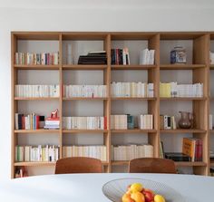 a dining room table with fruit on it and bookshelves in the back ground