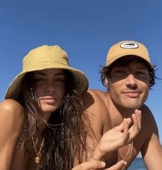 a man and woman laying on the beach with their arms around each other as they look at the camera