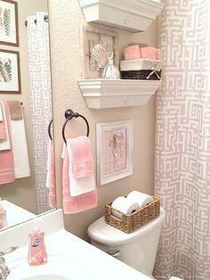 a white toilet sitting next to a bathroom sink under a mirror with pink towels hanging on it