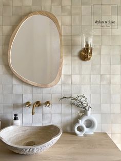 a bathroom sink sitting under a round mirror next to a vase with flowers in it