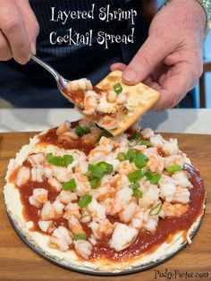 a person is spooning some food out of a small pizza on a plate with the words layered shrimp cocktail spread over it