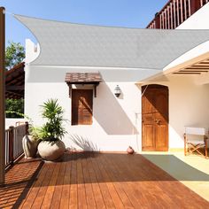 a wooden deck with potted plants on it next to a white wall and brown shutters