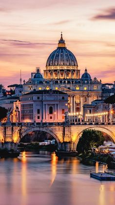 the dome of an old building is lit up at night in front of a body of water