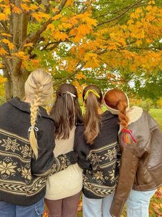 three girls standing in front of a tree with their backs to the camera, looking down