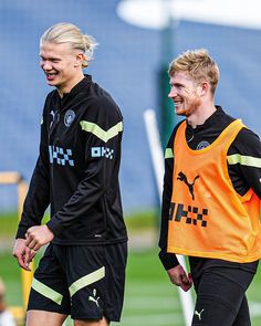 two soccer players are walking on the field with their hands in each other's pockets