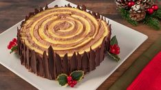 a chocolate cake on a white plate topped with frosting and christmas decorations next to pine cones