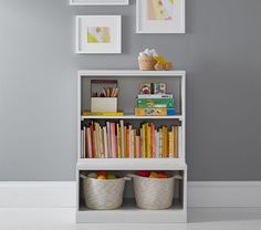 a white book shelf filled with books next to two baskets full of books and pictures on the wall