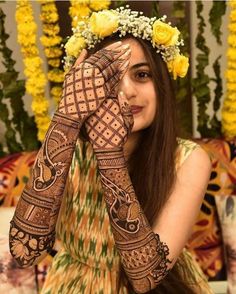 a woman with henna on her hands and yellow flowers in the hair is smiling at the camera