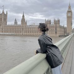 a woman is standing on a bridge looking at the water and big ben in london