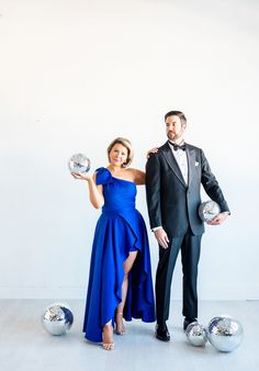 a man in a tuxedo and a woman in a blue dress holding disco balls