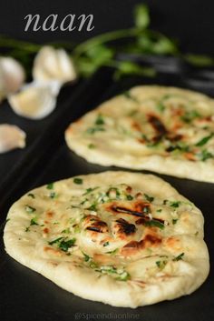 two flat bread pizzas sitting on top of a black tray next to garlic and green onions