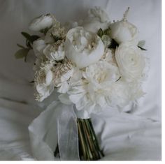 a bridal bouquet with white flowers and greenery on a bed in the background