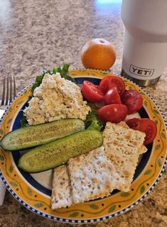 a plate with crackers, cucumbers and tomatoes on it next to an orange