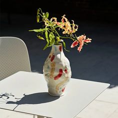 a vase filled with flowers sitting on top of a table next to a white chair