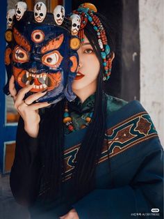 a woman holding up a mask with skulls on it's face and wearing headdress