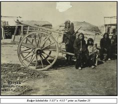 an old black and white photo of people standing next to a wagon with wheels on it