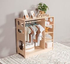 a wooden toy closet with clothes and other items on it's shelves next to a potted plant