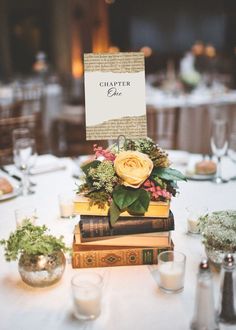 a table topped with books covered in flowers and greenery next to glasses filled with candles