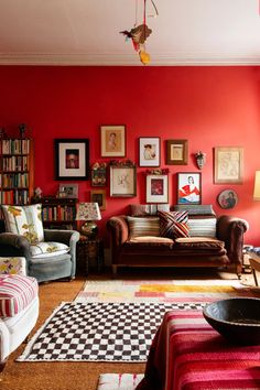 a living room filled with lots of furniture and pictures on the red wall above it